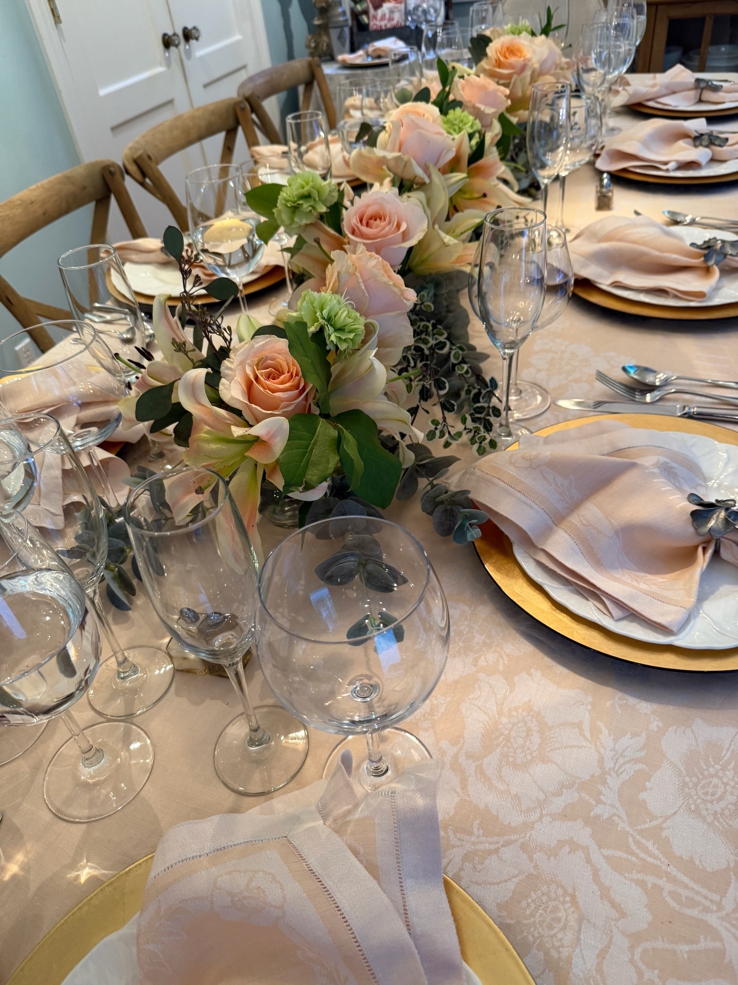 Close dining table view with peach roses, lilies and layered glassware