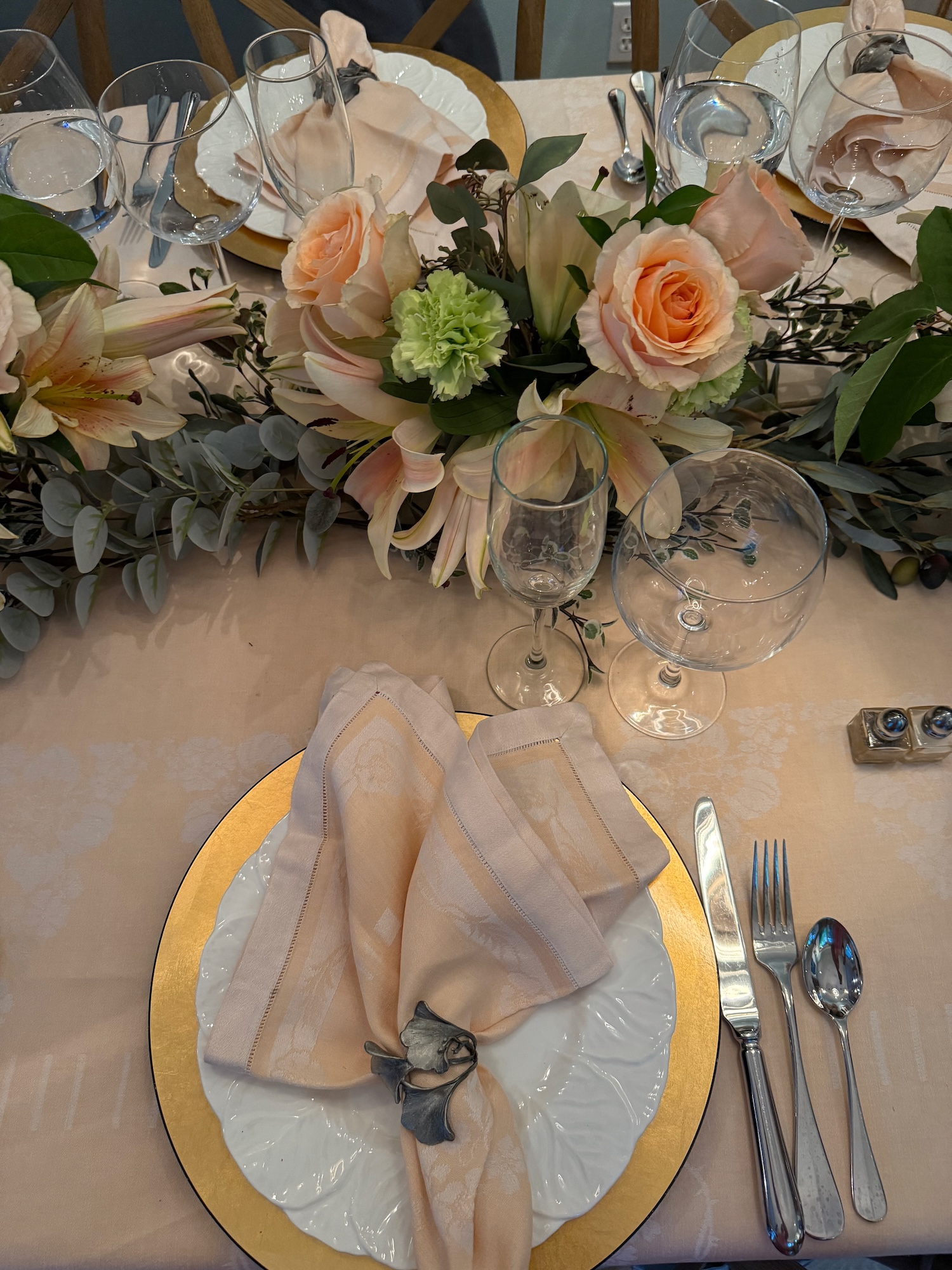 Place setting with peach napkin, gold charger and lush floral runner
