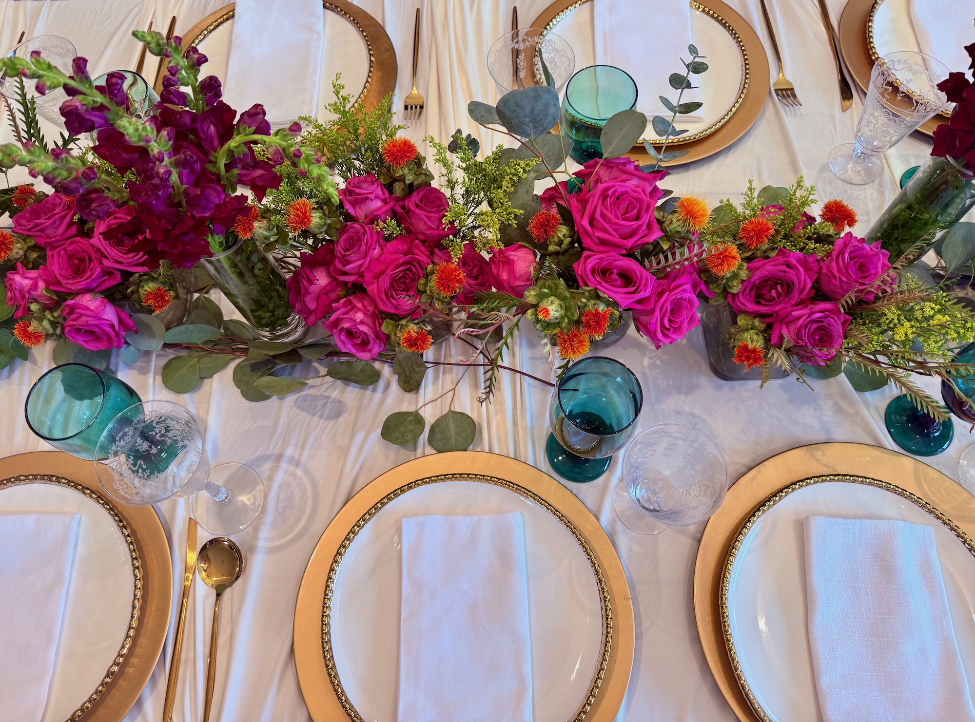 Overhead floral arrangement with vivid pink roses and teal glassware