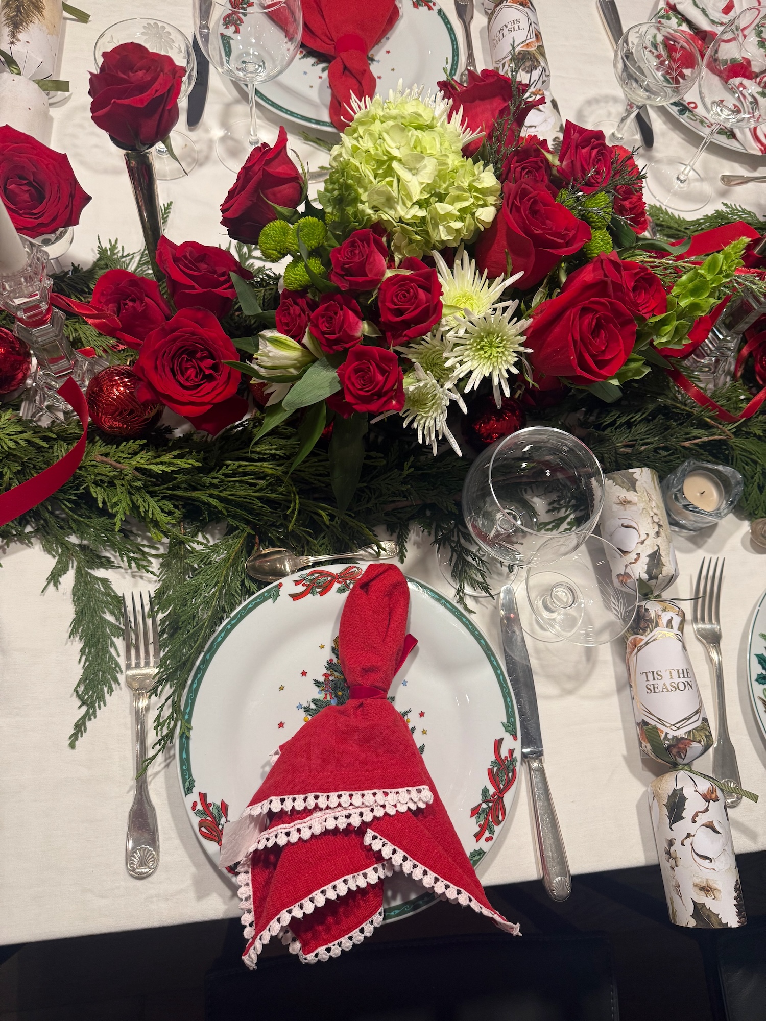 Holiday centerpiece detail with red roses, greenery and festive crackers