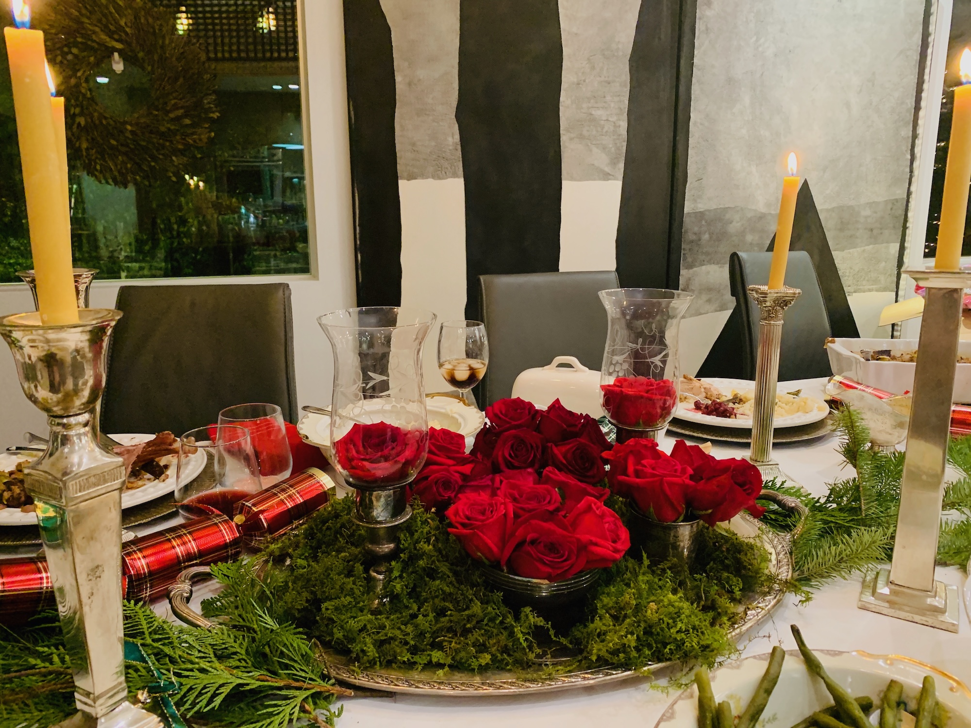 Candlelit holiday dinner table with red roses and moss centerpiece